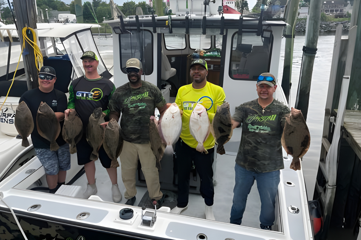 Five people on a boat holding flat, oval fish.