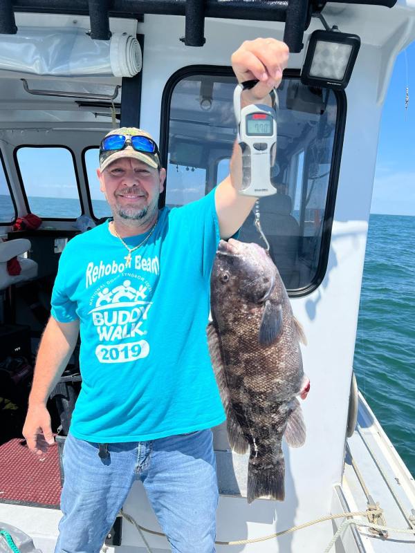 Man holding a large fish on a boat under a sunny sky.