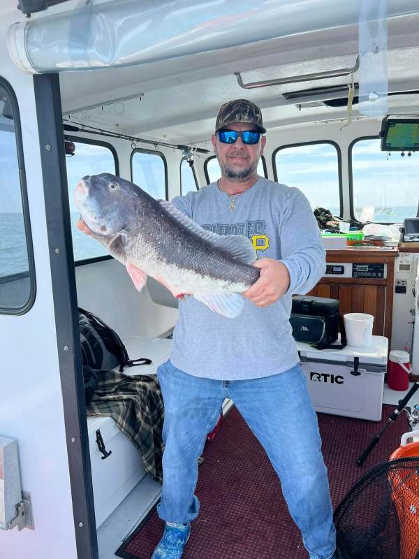 Man holding large fish on a boat, wearing sunglasses and a cap.