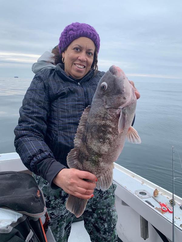 Person in a jacket and purple hat holding a large fish on a boat.