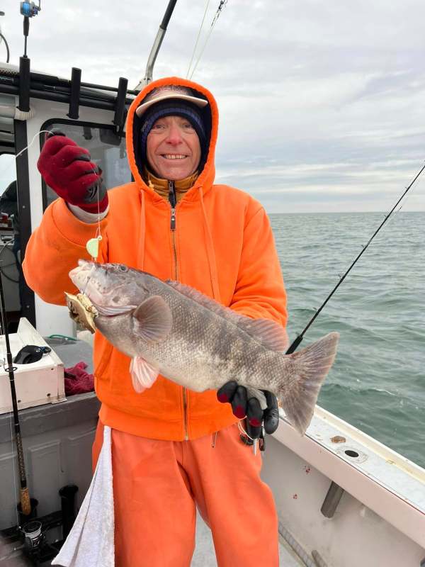 Person in orange hoodie holding a large fish on a boat.