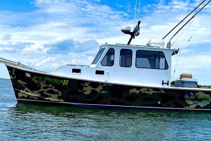 Camo-patterned fishing boat on water under a blue sky with clouds.