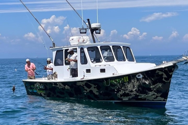 Three people fishing on a boat in the ocean.