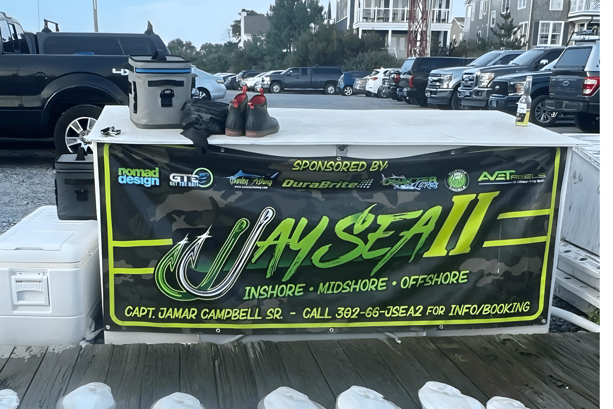 Fishing charter sign on a dock with nearby cars and houses.